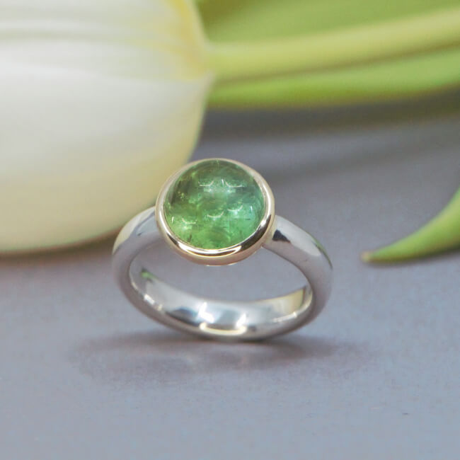 Ring aus Silber mit golden gefasstem grünen Stein.