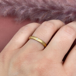 Der Trauring "Charlotte" in Gold mit kleinem Diamant am Ringfinger der linken Hand. 