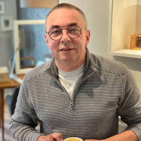 Detlef von den Schmuckgefährten hält eine Kaffeetasse in den Händen und lächelt in die Kamera.