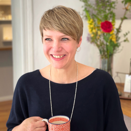 Elisabeth, die Inhaberin der Goldschmiede Schmuckgefährten hält eine Tasse Kaffee in der Hand und lacht. 