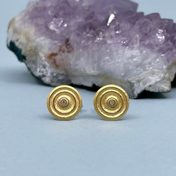 Ohrstecker "Emilia" aus 925 Silber und 585 Gelbgold Zwei Ohrstecker in Silber und Gelbgold mit Brillant liegen auf blauem Grund.