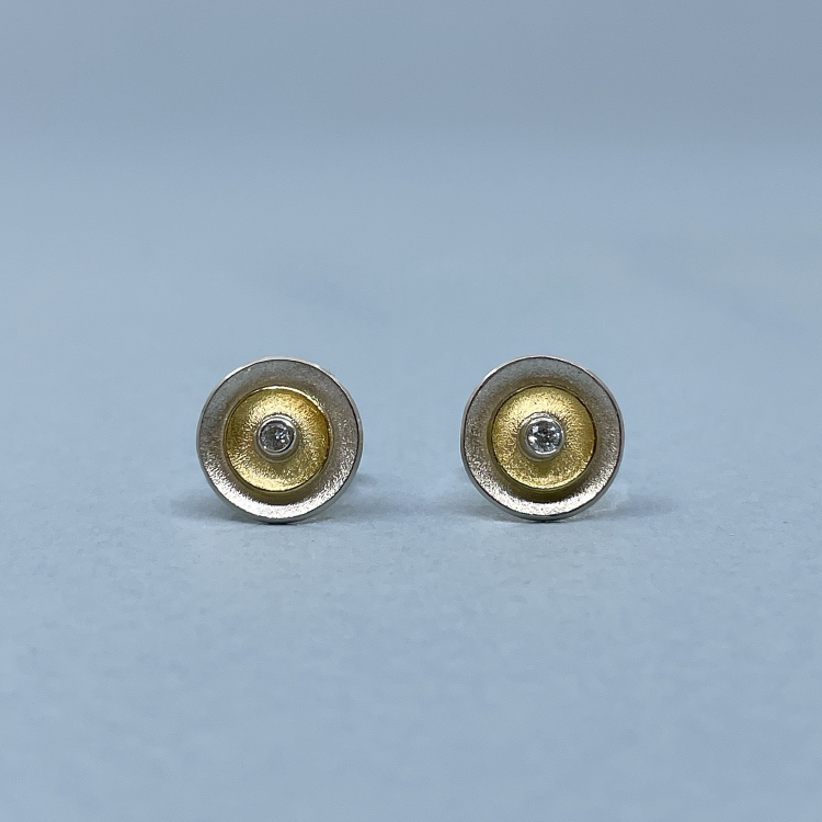 Ohrstecker "Laureen" aus 925 Silber und 585 Gelbgold Zwei Ohrstecker in Silber und Gelbgold mit Brillant liegen auf blauem Grund.